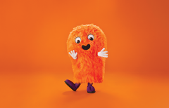 Oranssi, karvainen maskottihahmo vilkuttelee kokovartalokuvassa