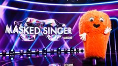 Oranssi, karvainen maskottihahmo vilkuttelee Masked Singer -ohjelman lavalla