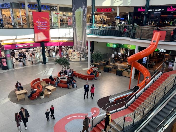 Kauppakeskus Myllyn yläkerrasta otettu kuva, jossa näkyy alakerrassa oleva Myllyntori, liukumäki, ihmisiä ja kauppakeskuksen liikkeitä.