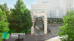 Sisäänkäynti valkoiseen rakennukseen vehreän ympäristön keskellä, edessä kaariportti. Alakulmassa teksti "Sustainable Travel Finland".