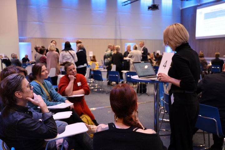Alt-teksti: Ihmiset keskustelevat pöytien ääressä seminaaritilassa.