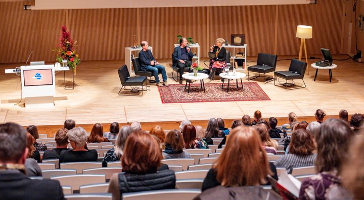 Paneelikeskustelu yleisön edessä suuressa auditoriossa. Lavalla on neljä henkilöä istumassa ja keskustelemassa.