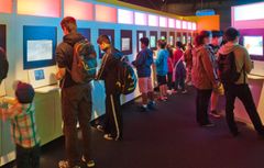 Henkilöitä pelaamassa videopelejä värikkäässä näyttelytilassa.