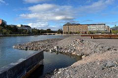John Stenbergin rantaa Helsingin Hakaniemessä. Etualalla on kivinen rantakaista ja taustalla rakennuksia.