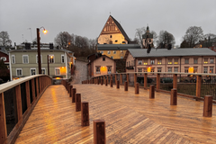 Puusilta Porvoon Vanhassa kaupungissa, taustalla värikkäitä puutaloja ja kirkko harmaassa säässä.