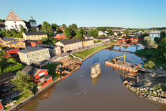 Ilmakuva Porvoosta kesällä. Etualalla sillanrakennustyömaa, jossa käytetään erikoisvalmisteltua lauttaa. Taustalla väliaikainen jalankulkusilta. ympärillä vehreää maisemaa ja värikkäitä taloja.
