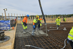 Rakennustyömaalla useita työntekijöitä valaa betonia teräskehikon päälle.