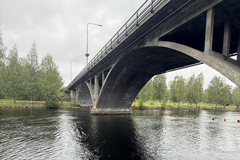 Silta ylittää rauhallisen joen, ympärillä vehreitä puita.