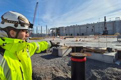 Mies keltaisessa takissa ja kypärässä osoittaa rakennustyömaata, jossa näkyy paalulaatta.