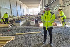 Työmaakuvassa keltatakkinen henkilö kypärä päässä seisoo raideasennustyömaalla. Taustalla näkyy muita työntekijöitä ja rautatiekiskoja.