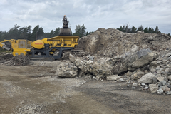 Betonimurskaa käsittelevä murskain työmaa-alueella suurten purkubetonikasojen vieressä.