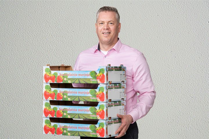 Mies pitää kädessään neljää aaltopahvista mansikkalaatikkoa