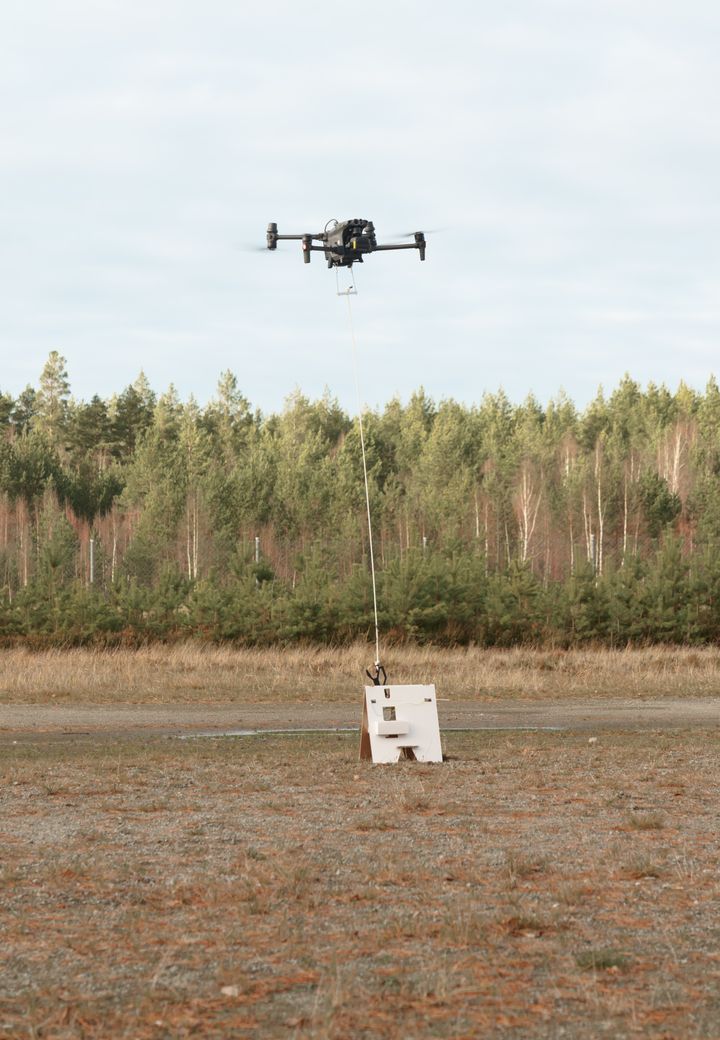 Drone jonka kyydissä aaltopahvinen tukijalka ja pahvipakkaus, joiden avulla miinanraivaus voidaan tehdä turvallisesti