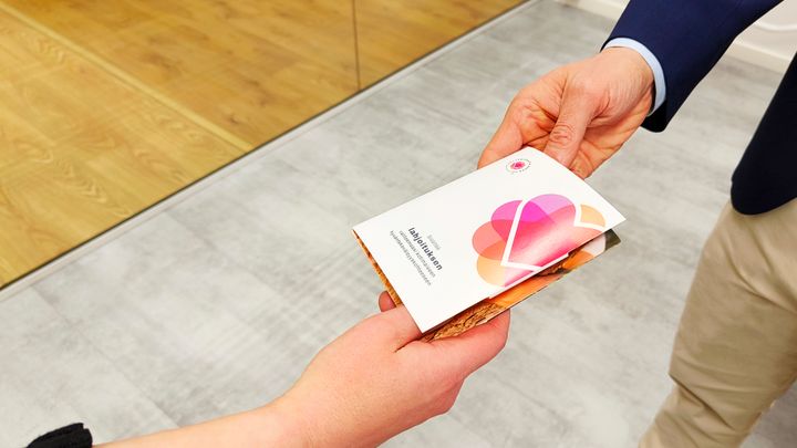 kuvassa kaksi kättä ja Auttamisesta arkea-hyväntekeväisyyslahjakortti