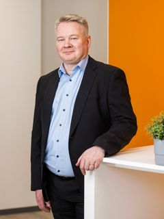 Mies seisoo pöydän vieressä puku päällä ja hymyilee kameralle