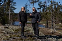 Kaksi henkilöä, nainen ja mies, ihastelevat metsäistä ympäristöä aurinkoisena päivänä kallion laella. Kuvan taustalla näkyy mäntymetsikköä ja vesistöä.