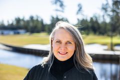 Kuvassa henkilö hymyilee kameralle ulkona. Taustalla näkyy vesistö ja metsää.