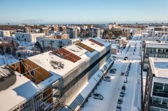 Ilmakuva talvisesta kaupunginosasta, jossa etualalla näkyy keskeneräinen moderni harjakattoinen rakennus.