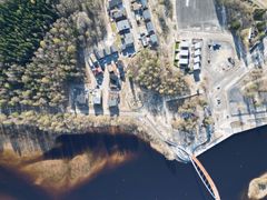 Ilmakuva Oulujoen suiston alueesta, jossa puurakennuksia, metsää ja silta.