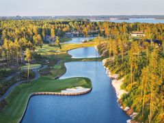 Ilmakuva golfkentästä, jossa on paljon puita, vettä ja erilaisia väyliä. Taustalla näkyy metsä ja vesistö.