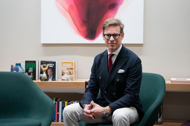 Jussi Mäkinen istuu vihreällä tuolilla. Vieressä toinen vihreä tuoli. Takana valkoinen Canvas-taulu, jossa punainen grafiikka.