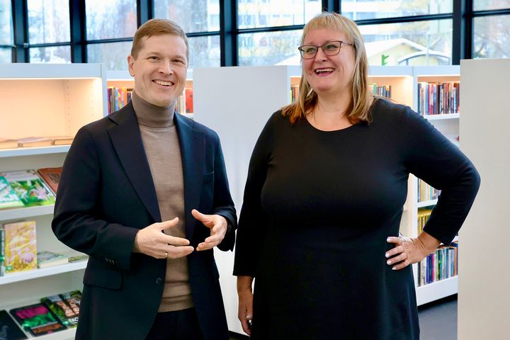 Two people smiling and standing in a library.