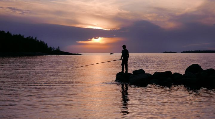 Auringonlasku, onkija seisoo rantakivikolla