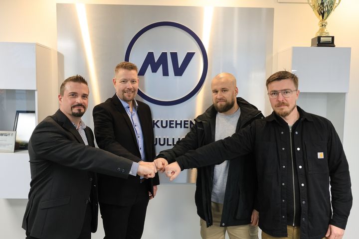 Neljä miestä lyö kätensä yhteen MV-Jäähdytyksen aulassa, MV-logon edessä.