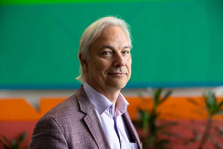 Potrettikuva Per Ashornista, jolla on yllään harmaa puvuntakki. Taustalla näkyy viherkasveja sekä vihreää ja oranssia seinää.