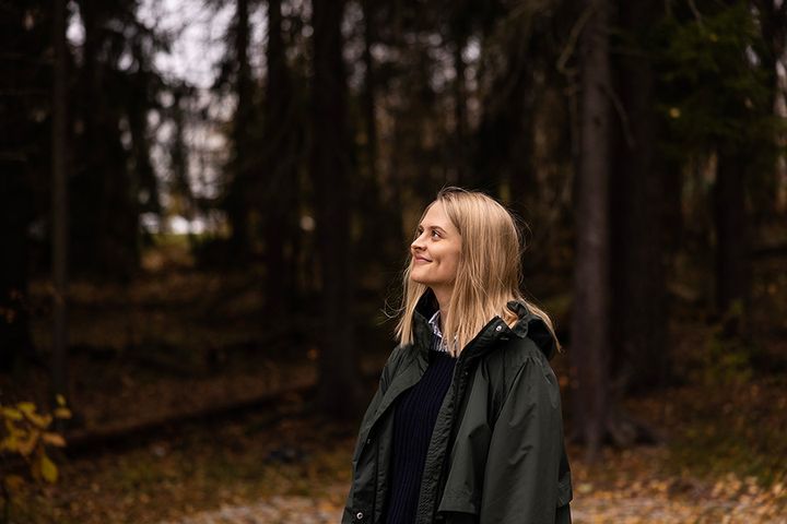 Puolivartalokuva Venla Kuusisesta, joka katsoo hymyillen sivuun kamerasta. Taustalla näkyy metsää.