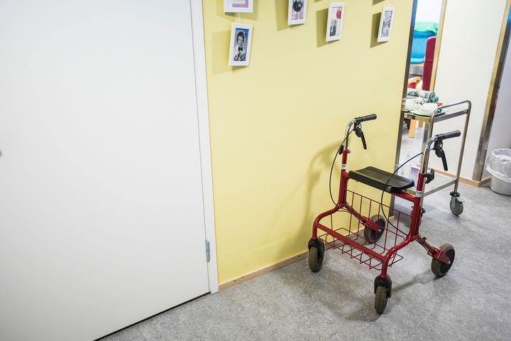 Punainen rollaattori käytävällä kellertävän seinän vieressä.
