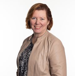 Nainen beige takki päällä hymyilee kameralle. Teksti: Väitöskirjatutkija Mervi Huhtelin.
