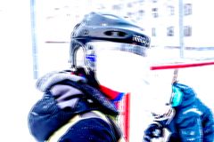 Lapsi jääkiekkokypärässä seisoo ulkona kirkkaassa valossa. Taustalla on maalivahti.