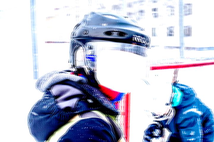 Lapsi jääkiekkokypärässä seisoo ulkona kirkkaassa valossa. Taustalla on maalivahti.