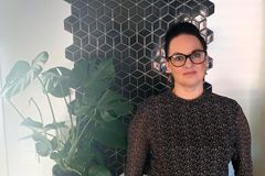 Henkilö seisoo seinän edessä, jossa on musta geometrinen kuvio. Vieressä on viherkasvi.