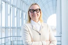 Nainen, joka hymyilee kameralle modernissa lasikäytävässä.