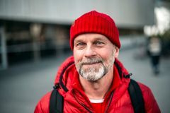 Mies punaisessa pipossa ja takissa hymyilee katsoen kameraan.