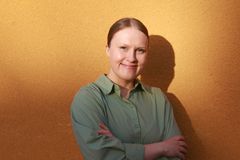 Henkilö seisoo poikittain keltaista seinää vasten, kädet ristittyinä, katsoen kameraan hymyillen.