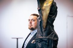 Mies seisoo katsoen kameraan, suuri patsas edessään.