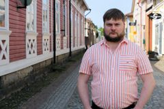 Punavalkoraidalliseen paitaan pukeutunut henkilö seisoo kadulla, jonka varrella on vanhoja puisia taloja.