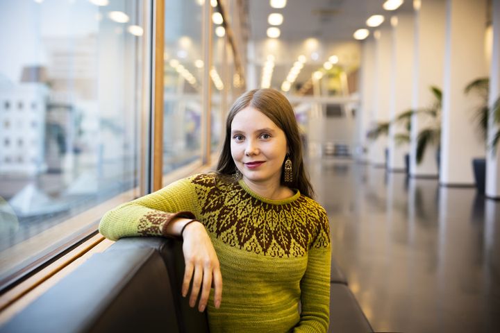 En kvinna sitter i en soffa i en modern lobby, klädd i en dekorerad grön tröja.