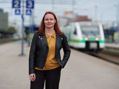 Tiia Loponen seisoo rautatieasemalla ja taustalla näkyy juna.