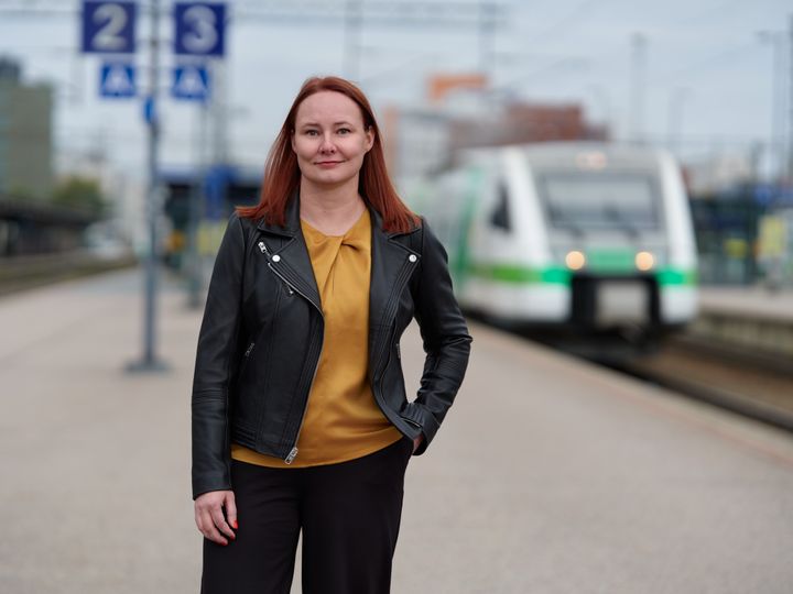 Tiia Loponen seisoo rautatieasemalla ja taustalla näkyy juna.
