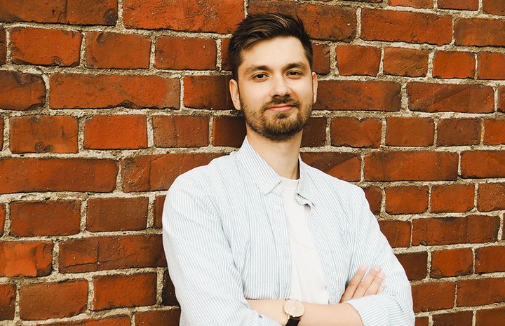 Mies nojaa tiiliseinään, kädet ristittynä rinnalleen.