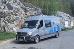 Harmaaseen pakettiautoon rakennettu mobiililaboratorio pysäköitynä levähdyspaikalla kallioleikkauksen vieressä.