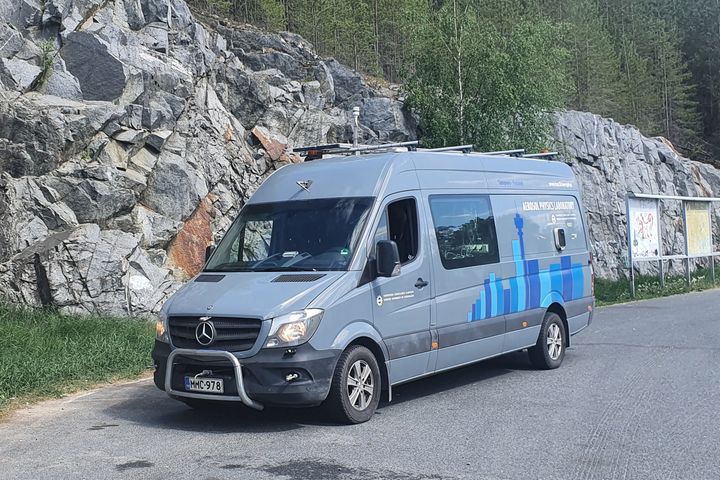 Harmaaseen pakettiautoon rakennettu mobiililaboratorio pysäköitynä levähdyspaikalla kallioleikkauksen vieressä.