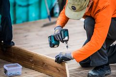 Henkilö rakennustyömaalla asentaa puulevyä akkuporakoneella.