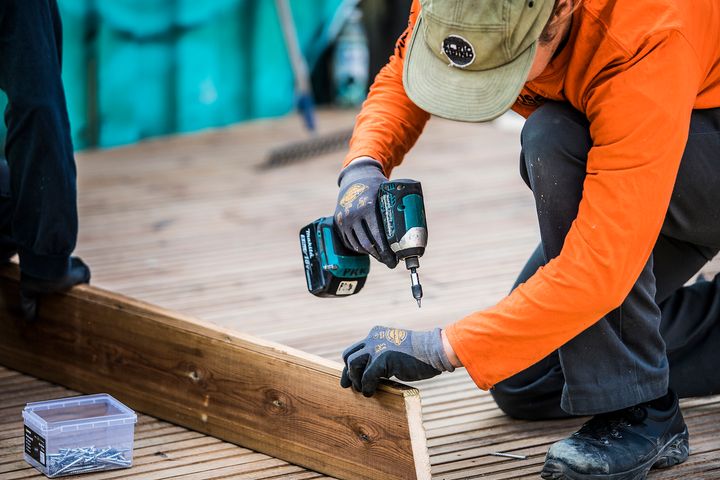 Henkilö rakennustyömaalla asentaa puulevyä akkuporakoneella.
