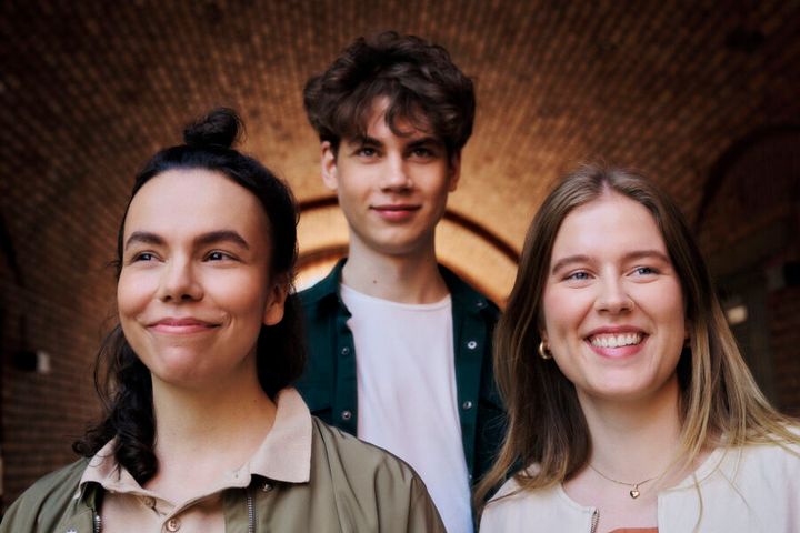 Kolme hymyilevää henkilöä seisoo tunnelissa.