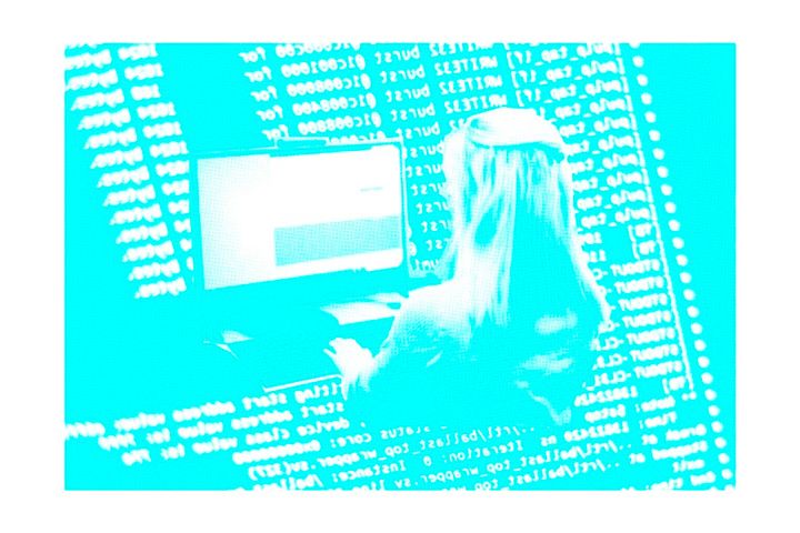 Henkilö istuu tietokoneen ääressä, ruudulla ohjelmointikoodia.